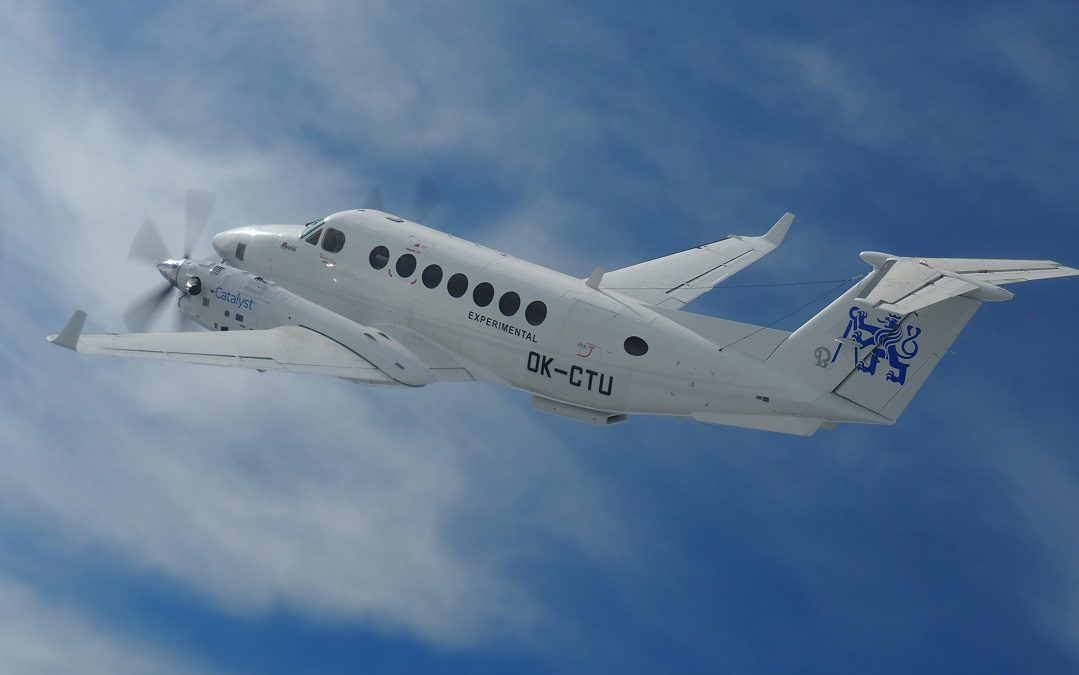 A white twin-engine aircraft with NASA branding on its tail flying through a bright blue sky with scattered clouds. The aircraft features a sleek design and is captured mid-flight, showcasing its wings and engines.