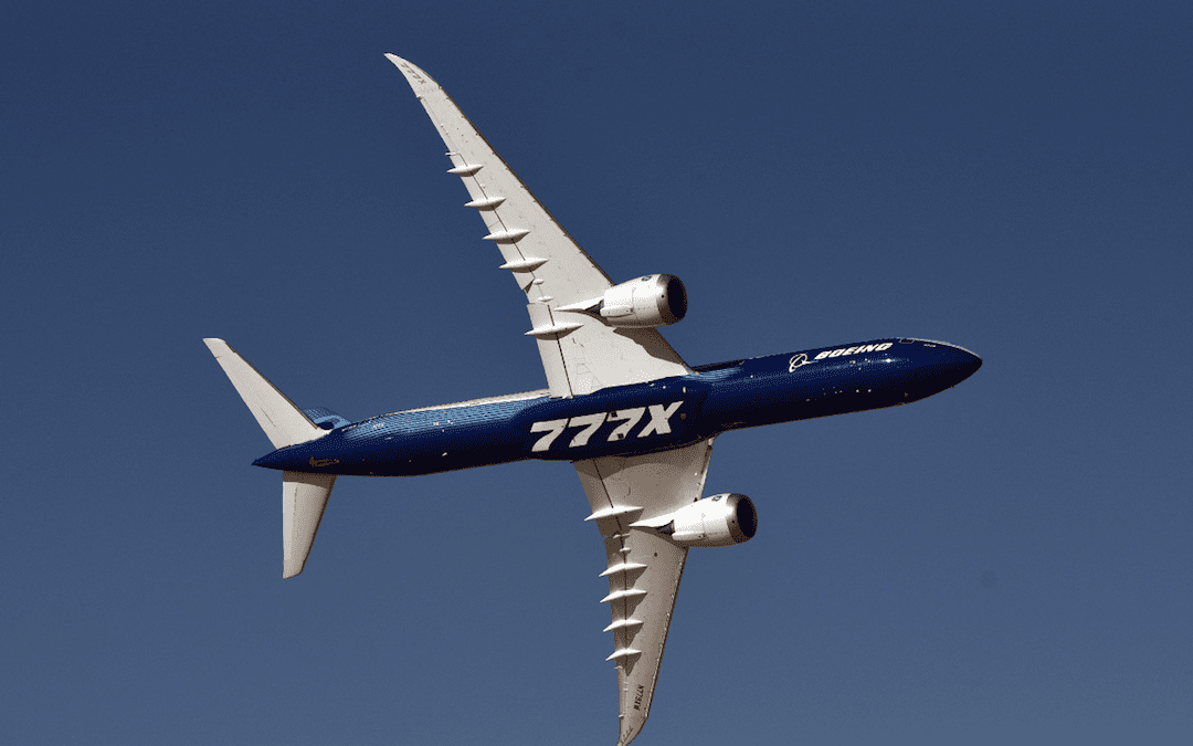 A Boeing 787 Dreamliner with a blue livery soars through a clear blue sky, showcasing its sleek design and curved wings.